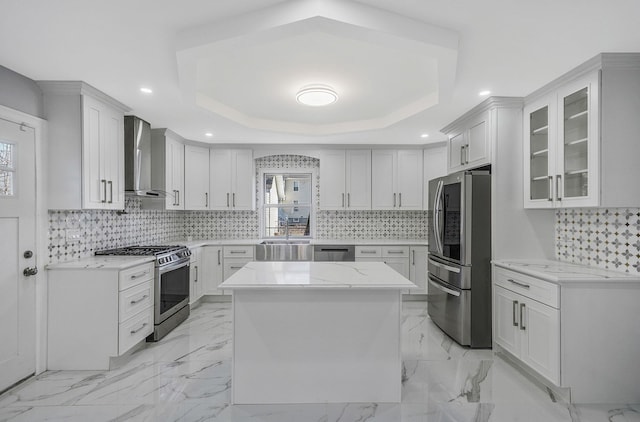 kitchen with a tray ceiling, white cabinetry, stainless steel appliances, and wall chimney range hood