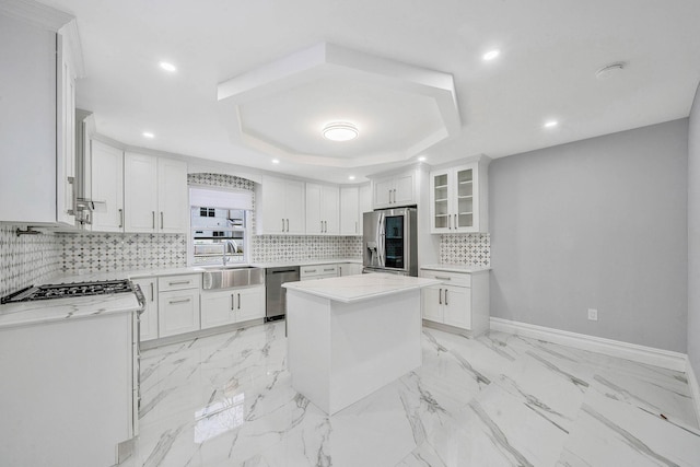 kitchen featuring a raised ceiling, sink, appliances with stainless steel finishes, a kitchen island, and white cabinetry