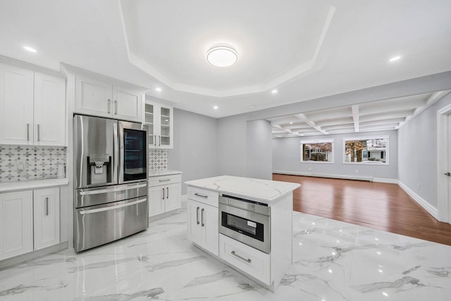 kitchen with tasteful backsplash, light stone counters, stainless steel appliances, white cabinets, and a center island