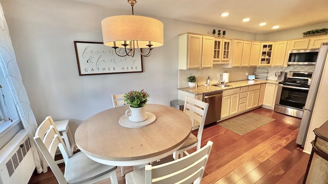 kitchen featuring decorative backsplash, decorative light fixtures, light stone counters, radiator heating unit, and stainless steel appliances