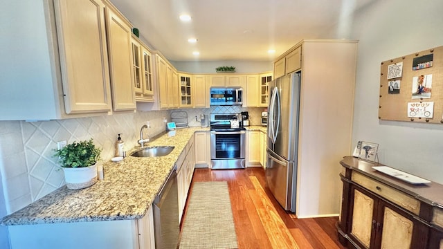 kitchen featuring light stone countertops, tasteful backsplash, stainless steel appliances, sink, and light hardwood / wood-style flooring