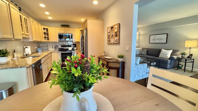 kitchen with light stone countertops, sink, stainless steel appliances, backsplash, and light brown cabinetry