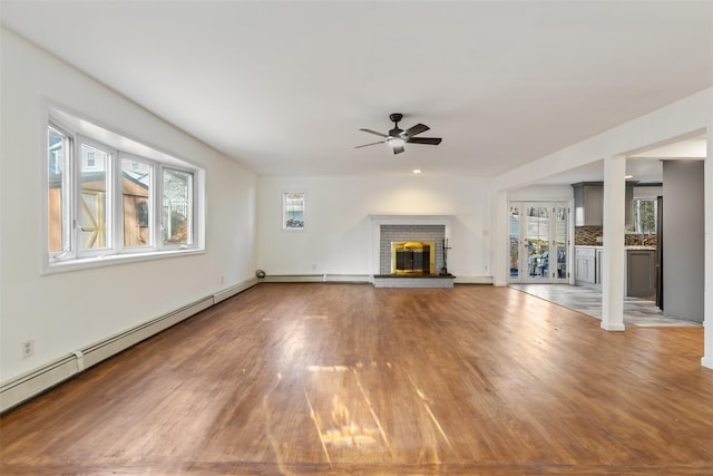 unfurnished living room featuring a fireplace, plenty of natural light, baseboard heating, and ceiling fan