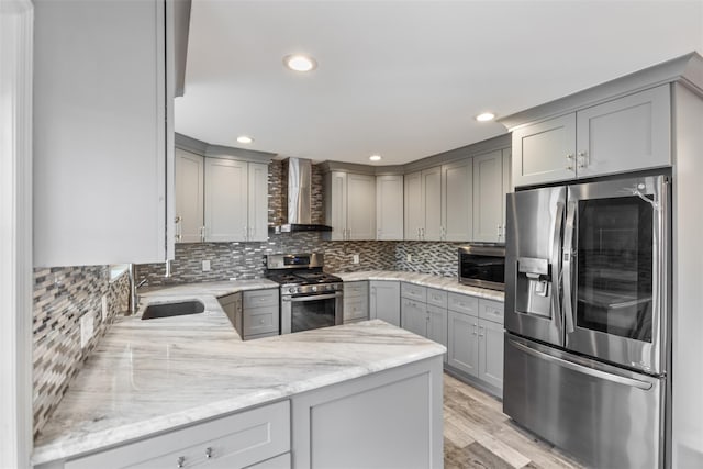 kitchen featuring gray cabinetry, sink, wall chimney exhaust hood, stainless steel appliances, and light stone counters