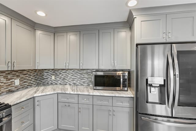 kitchen featuring backsplash, gray cabinets, light stone counters, and appliances with stainless steel finishes