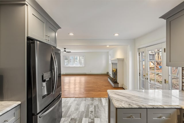 kitchen featuring gray cabinetry, light stone countertops, ceiling fan, stainless steel refrigerator with ice dispenser, and light hardwood / wood-style floors