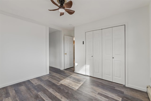 unfurnished bedroom with ceiling fan, baseboard heating, dark wood-type flooring, and a closet