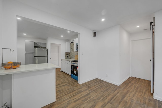 kitchen featuring white cabinets, dark hardwood / wood-style floors, a barn door, appliances with stainless steel finishes, and tasteful backsplash