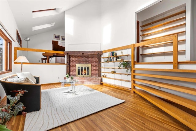 living area featuring a skylight, a fireplace, high vaulted ceiling, and wood finished floors