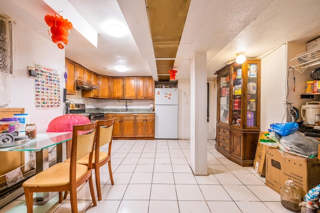 kitchen featuring a textured ceiling, light tile patterned floors, stainless steel gas stove, white fridge, and range hood