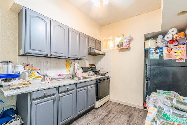 kitchen featuring sink, white range with gas stovetop, backsplash, stainless steel fridge, and light hardwood / wood-style floors