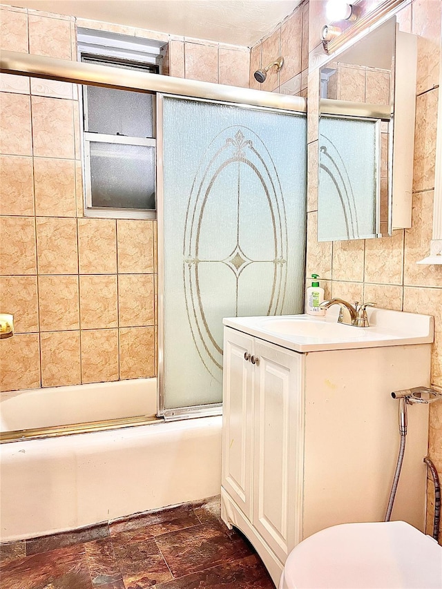 full bathroom featuring vanity, bath / shower combo with glass door, tile walls, and toilet