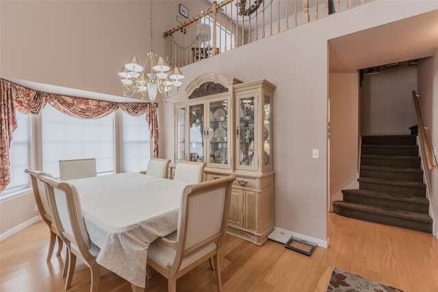 dining area with light hardwood / wood-style floors, a high ceiling, and an inviting chandelier