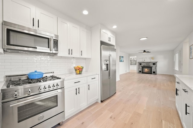 kitchen with a stone fireplace, ceiling fan, stainless steel appliances, light stone countertops, and white cabinets