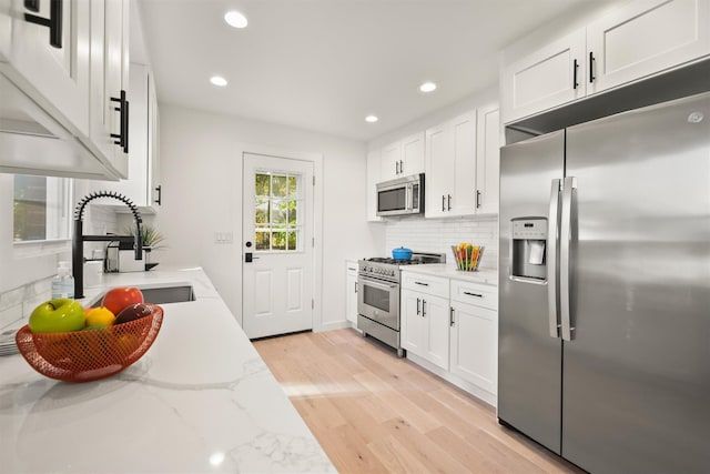 kitchen with stainless steel appliances, white cabinets, light stone counters, and sink