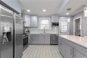 kitchen with gray cabinetry, sink, hanging light fixtures, appliances with stainless steel finishes, and light wood-type flooring