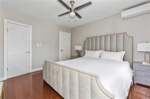 bedroom with a wall mounted air conditioner, ceiling fan, and dark hardwood / wood-style flooring