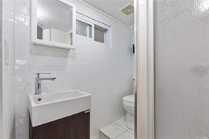 bathroom featuring vanity, toilet, and tile walls