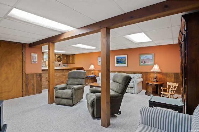 living room featuring a drop ceiling, wood walls, and light colored carpet