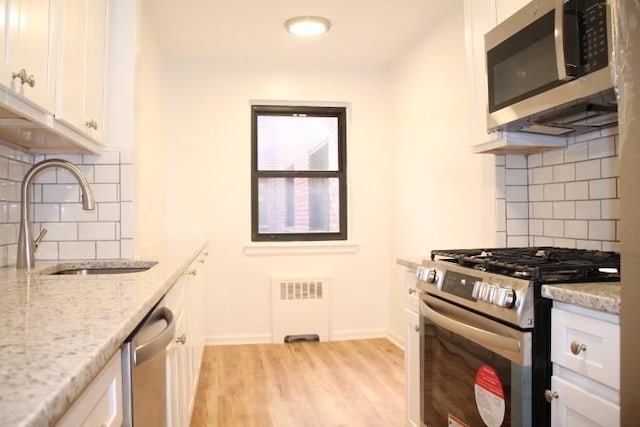 kitchen with light stone countertops, appliances with stainless steel finishes, sink, radiator heating unit, and white cabinetry