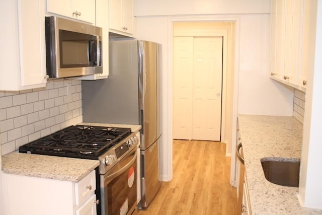 kitchen with white cabinets, decorative backsplash, light stone countertops, and stainless steel appliances