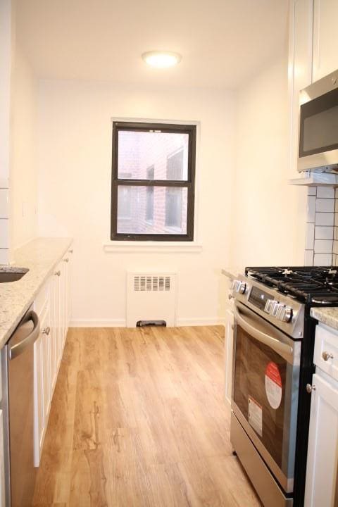 kitchen featuring white cabinets, radiator heating unit, and stainless steel appliances