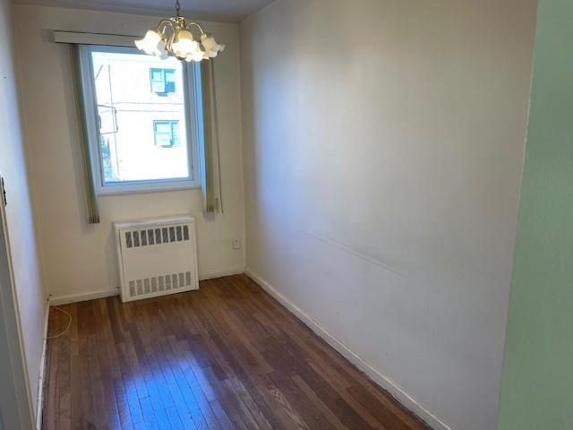 unfurnished room featuring radiator, dark wood-type flooring, and a notable chandelier