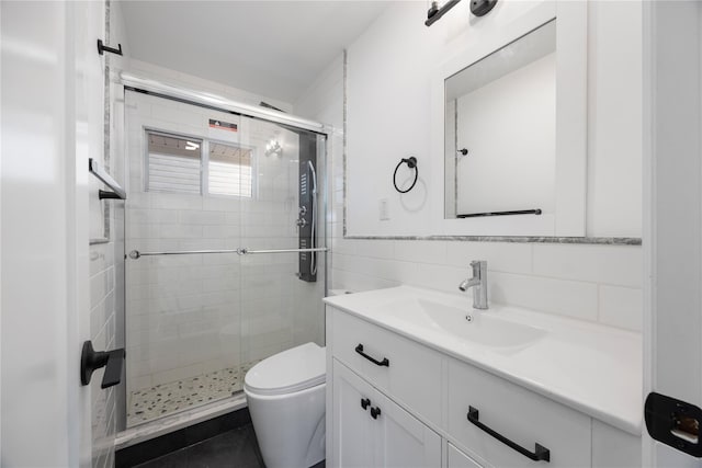 bathroom with tile patterned floors, toilet, a shower with door, vanity, and tile walls