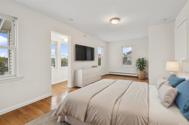 bedroom featuring multiple windows, light hardwood / wood-style flooring, and a baseboard heating unit