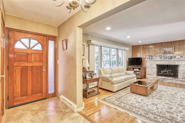 foyer featuring a stone fireplace, a baseboard heating unit, and an inviting chandelier