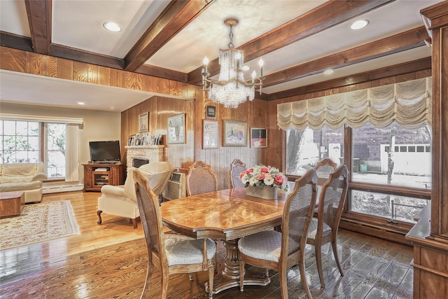 dining area with beamed ceiling, wood walls, a fireplace, and hardwood / wood-style flooring