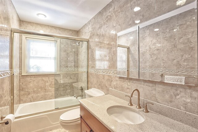 bathroom with combined bath / shower with glass door, toilet, tile walls, and vanity