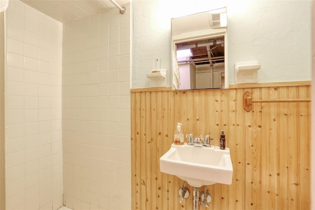 bathroom featuring a wainscoted wall, wooden walls, and a tile shower