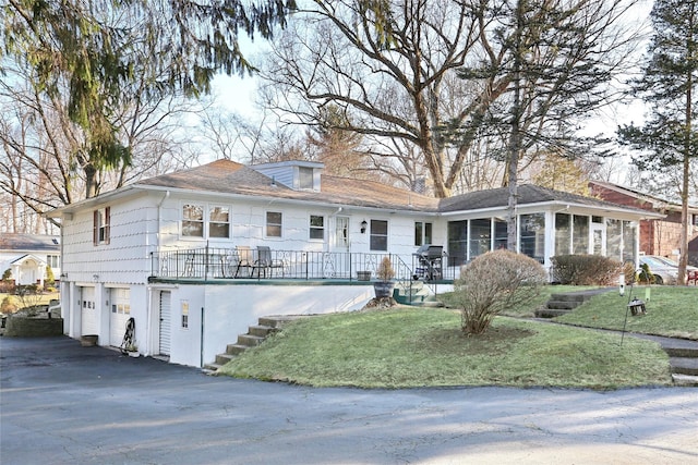 view of front of house featuring an attached garage, a sunroom, stairs, a front lawn, and aphalt driveway