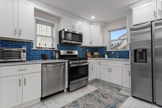 kitchen with decorative backsplash, appliances with stainless steel finishes, sink, white cabinets, and plenty of natural light