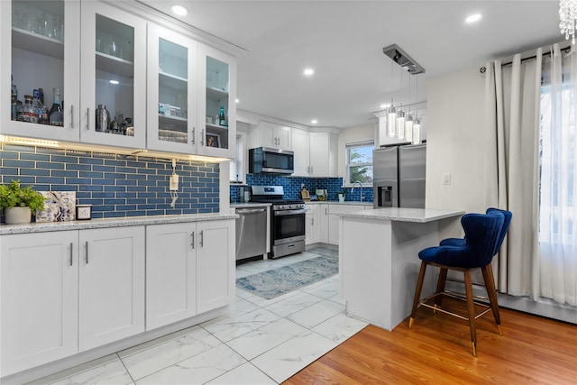 kitchen with light stone countertops, white cabinetry, appliances with stainless steel finishes, and tasteful backsplash