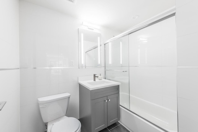 full bathroom featuring tile patterned floors, bath / shower combo with glass door, vanity, tile walls, and toilet