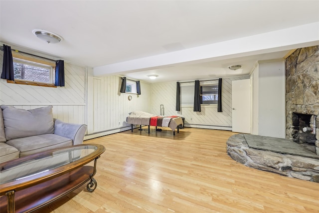 living room with a fireplace, light hardwood / wood-style flooring, baseboard heating, and wooden walls