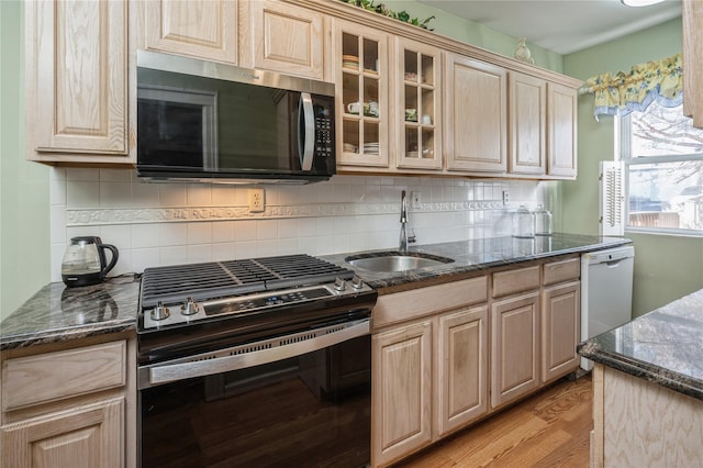 kitchen with dark stone counters, sink, light wood-type flooring, tasteful backsplash, and stainless steel appliances