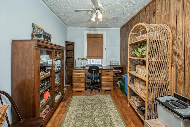 office area with a textured ceiling, ceiling fan, crown molding, dark wood-type flooring, and wood walls