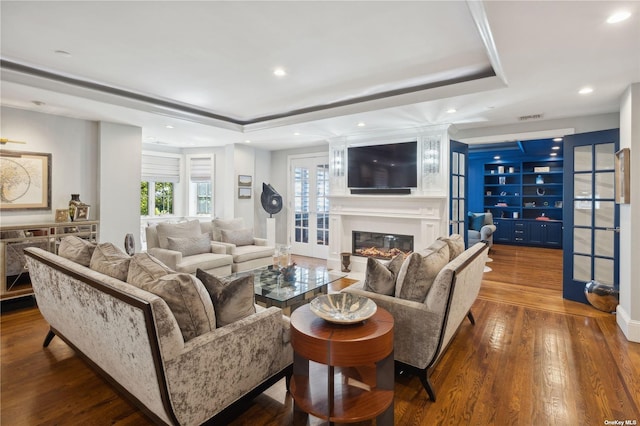 living room with a raised ceiling, dark hardwood / wood-style flooring, a large fireplace, and french doors