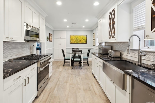 kitchen featuring dark stone counters, white cabinets, crown molding, sink, and appliances with stainless steel finishes