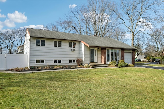 split level home with a garage, a shingled roof, aphalt driveway, fence, and a front yard