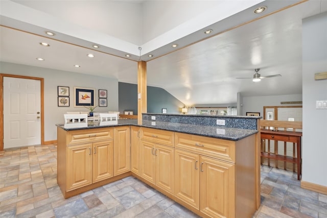 kitchen with kitchen peninsula, ceiling fan, and dark stone countertops