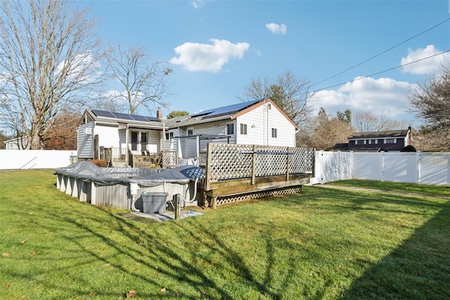 rear view of house with solar panels, a yard, and a swimming pool side deck