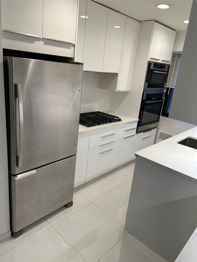 kitchen with tasteful backsplash, gas stovetop, white cabinetry, oven, and stainless steel refrigerator