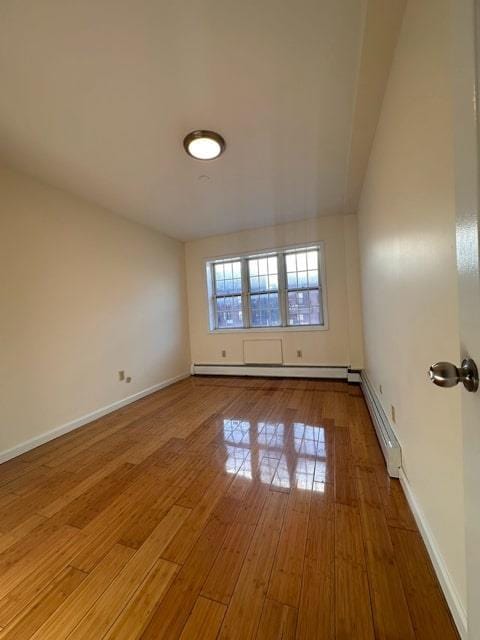 spare room featuring baseboard heating and hardwood / wood-style flooring