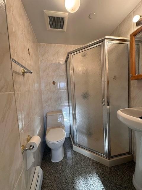 bathroom with toilet, baseboard heating, tile walls, and a shower with shower door