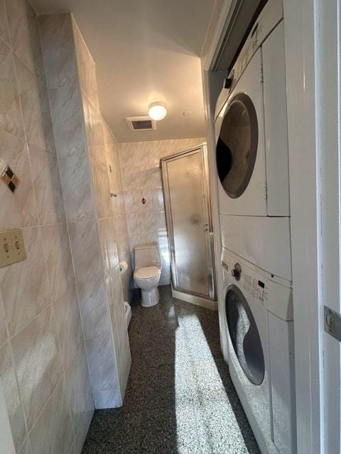 washroom featuring stacked washer and dryer and tile walls