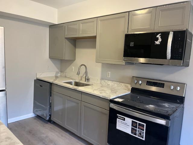 kitchen featuring sink, light stone counters, hardwood / wood-style floors, gray cabinets, and appliances with stainless steel finishes